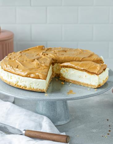 Cheesecake mit Dalgona Topping auf einer Tortenplatte, angeschnitten.