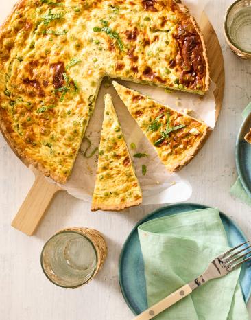 Erbsen Tarte auf einem gedeckten Tisch, in Stücke geschnitten, auf Tellern serviert.