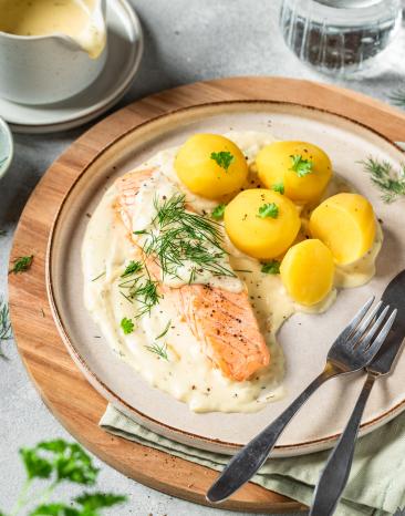 Lachsfilet in Senfsauce mit Kartoffeln auf einem Teller mit Saucière.