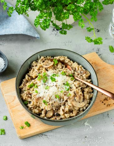 Pilzrisotto mit Parmesan in einer Schüssel auf einem Brettchen.