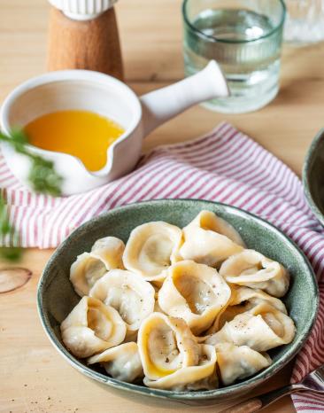Kleine Teigtaschen (Pelmeni vegetarisch) auf einem dunklen Teller.