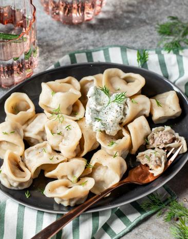 Pelmeni, gefaltete Teigtaschen, auf einem schwarzen Teller.