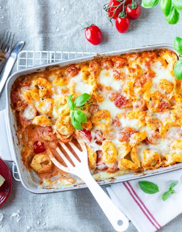 Tortelliniauflauf Tomate-Mozzarella in einer Auflaufform mit frischem Basilikum getoppt.