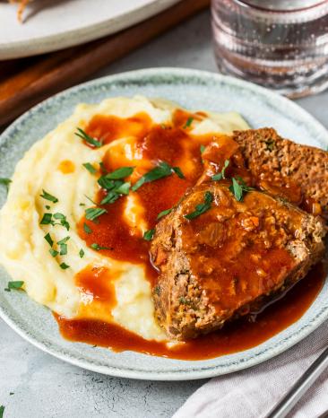 Hackbraten mit Sauce und Kartoffelpüree auf einem Teller und Braten im Ganzen.