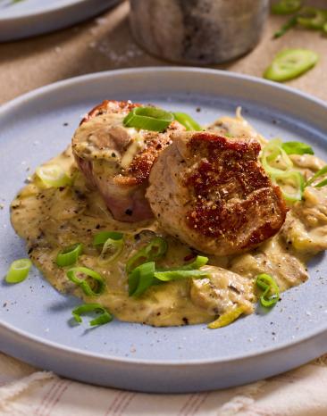 Schweinemedaillons mit Champignonsauce auf flachen Tellern angerichtet.