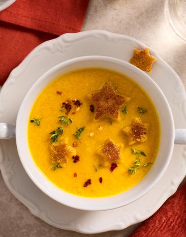 Gelbe Weihnachtssuppe mit Einlage in Schüsseln auf einem festlich gedeckten Weihnachtstisch.