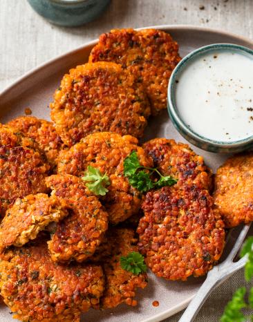 Linsenbratlinge mit Joghurtdip auf einer Platte.