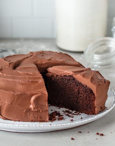 Veganer Schokokuchen mit Schokoladenfrosting aus der Springform auf einem Kuchenteller, angeschnitten.