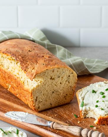 Kartoffelbrot angeschnitten auf einem Holzbrett, Scheibe bestrichen mit Kräuterbutter.