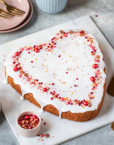 Rührkuchen in Herzform mit Glasur und rosa roten Zuckerstreuseln.