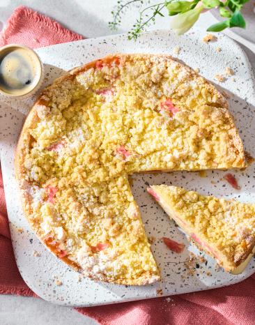 Rhabarberkuchen mit Pudding und Streuseln auf einem frühlingshaften Kaffeetisch.