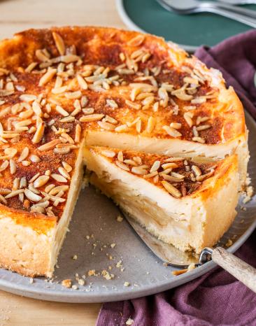 Apfel-Schmand-Kuchen mit Mandelstiften getoppt und ein Stück angeschnitten.