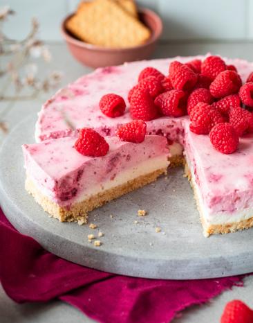 Himbeer-Frischkäse-Torte mit frischen Himbeeren getoppt und angeschnitten.