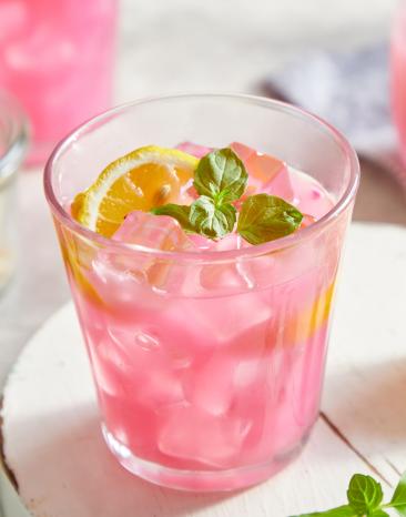 Pinke Zitronenlimonade in Gläsern serviert mit Eiswürfeln, Minze und Zitronenscheiben.