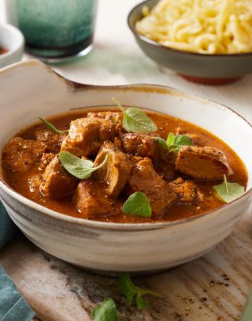 Schweinegulasch in einer Schüssel mit Kräutern getoppt.
