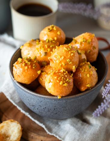 Loukoumades (Griechische Honigbällchen) in einer Schüssel mit Kaffee auf de Tisch.