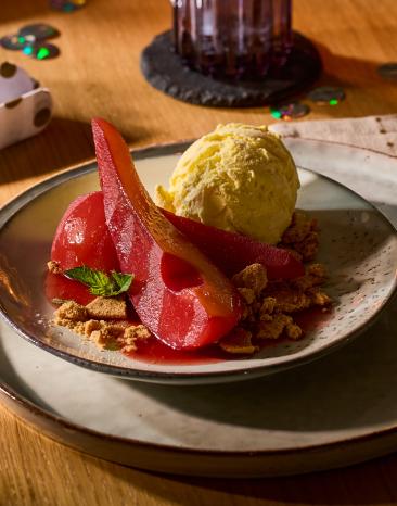 In Rotwein eingekochte Birnen mit weihnachtlichen Gewürzen wie Zimt und Sternanis mit einer Kugel Vanilleeis auf dem Teller.