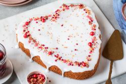 Rührkuchen in Herzform mit Glasur und rosa roten Zuckerstreuseln.